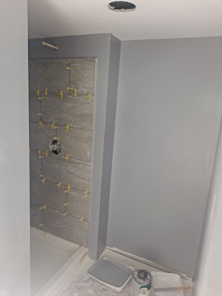Shower tile installation in progress with spacers next to freshly painted gray walls