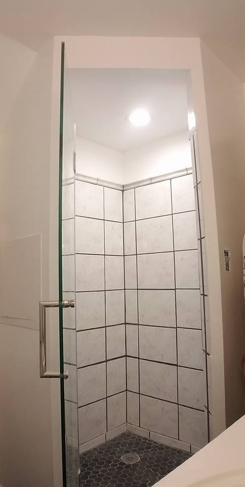 Completed white tile shower with glass door and hex tile floor